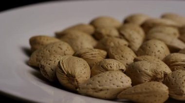 Kabuklu çiğ badem fıstıklarının yan görüntüsü. Beyaz bir tabakta, arka planda oturuyorlar. Yemeğin doğal ahşap dokusunu vurguluyorlar.