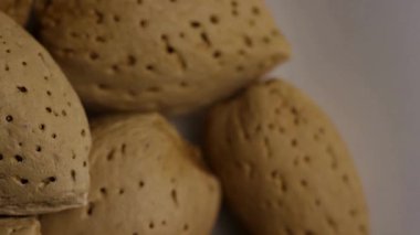 Sert kabuklarındaki bademlerin genel görünümü, doğal dokuyu ve detayı gösteren beyaz bir zemin üzerinde yavaşça dönüyor.