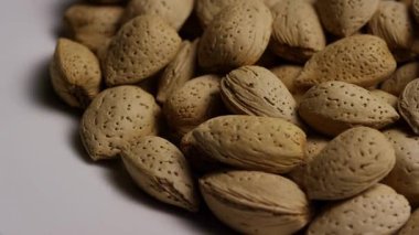 Temiz beyaz zemin üzerinde izole edilmiş kahverengi desenli kabuklu organik ham badem yığınlarının yakın çekim görüntüleri.