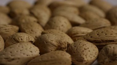 Kabuklu çiğ badem fıstıklarının yoğun arkaplanındaki yavaş çekimler kahverengi yüzeyleri ve doğal detayları gösteriyor.