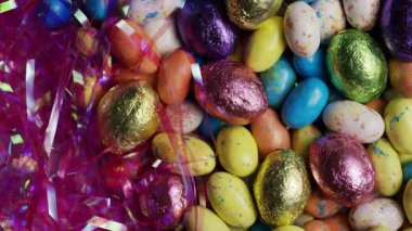 Değişen çikolata yığını renkli folyo ve benekli kabuklu Paskalya yumurtaları. Pembe tatil süslemeleri arka plan desenini kutluyor.