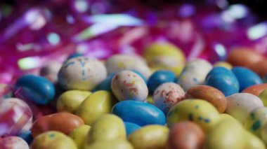 Düşük açılı, benekli pastel çikolatalı Paskalya yumurtaları. Tatil ve parti konsepti için parlak pembe süslemeli bokeh arka planı var.