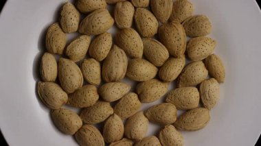 Yukardan aşağıya beyaz tabakta dönen kabuklu çiğ bademlerin beslenme ve beslenme için sağlıklı atıştırmalık malzemeleri.