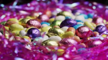 Renkli folyo sarılı mini çikolatalı paskalya yumurtaları. Pembe plastik çimlere gömülü. Bayram kutlamaları için yavaşça dönüyorlar.