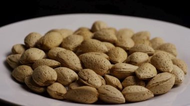 Beyaz tabakta dönen bir yığın organik badem fıstığı siyah arka planda izole edilmiş sağlıklı vejetaryen atıştırmalığı ve çiğ gıda konsepti.