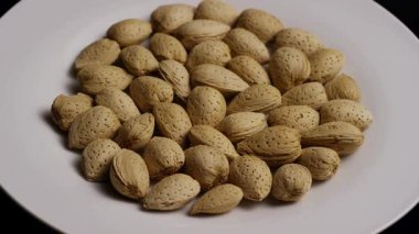 Sağlıklı Vejetaryen Diyet İçin Siyah Fındık Atıştırmalığına Karşı Beyaz Tabakta Kabuklu Doğal Bademlerin Dönen Yığını Kapat