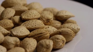 Beyaz tabakta bütün badem kabuklarını döndürerek dokulu kahverengi yüzeyi sağlıklı organik çerez ve doğal protein kaynağını gösterir.