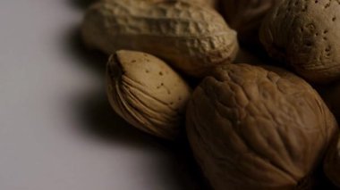 Makro, beyaz arka planda dönen kabuklu fıstık, fıstık ve ceviz de dahil olmak üzere karışık fındık çeşitliliğini ve dokusunu gösterir.