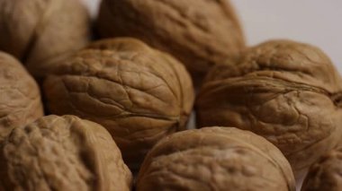 Sonbahar hasadı konsepti çekimi için beyaz yüzeyde yavaşça dönen buruşuk desenli kabuklu cevizlerin detaylı görüntüsünü kapat.