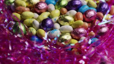 Bayram partisi için arka plan klipsleri olarak pembe yuvada çikolata ve şeker kaplı şeker içeren lezzetli paskalya ziyafetleri yığını.