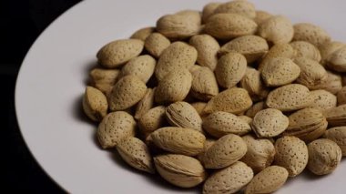 Kabuklu badem yığını beyaz tabakta siyah arka planda dönüyor sağlıklı organik çerez sunum stüdyosu kahverengi desenli fındıkları izole ediyor.