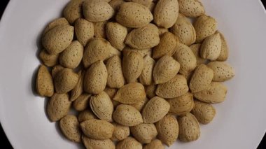 Sağlıklı vejetaryen protein kaynağı ve diyet konseptini temsil eden beyaz tabakta dönen badem kabuklarıyla dolu bir stüdyo resmi.