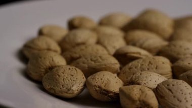 Beyaz bir tabakta bütün bademlerin yan görüntüsü yavaşça dönerek dokuyu ve şekli vurguluyor.