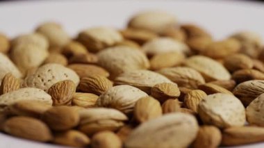 Karışık kabuklu ve kabuksuz badem fıstıkları sağlıklı atıştırmalıklar ve organik gıda konsepti için beyaz tabakta döner.