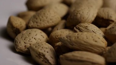 Sağlıklı abur cubur ve vejetaryen diyet kavramları için beyaz zemin üzerinde dönen kabuklu organik badem görüntülerini kapat