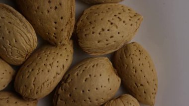 Sağlıklı atıştırma ve vejetaryen diyet kavramları için beyaz tabakta dönen kabuklu çiğ badem manzarasını kapat.