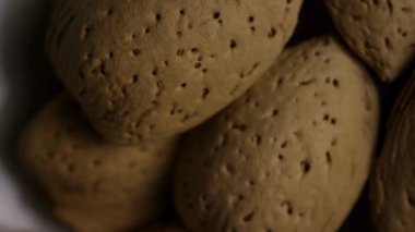 Kahverengi kabuklu çiğ organik badem yığınının makro görüntüsünü kapat. Detaylı dokuları ve doğal besin bileşenlerini yavaş yavaş göster.