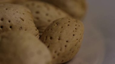 Makro, beyaz tabakta yavaşça dönen kahverengi kabuklu çiğ organik badem ve sağlıklı atıştırmalık yiyeceklere yakından bak.