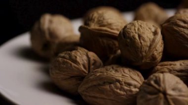 Kalıplı kahverengi kabuklu cevizler, beyaz bir tabakta siyah arka planda dönüyor. Yakın plan stüdyo görüntüsü.