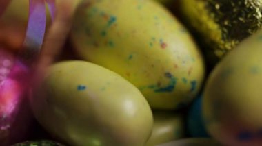 Sarı benekli paskalya yumurtaları ve pembe kurdeleli parlak folyolar yumuşak ışıkta dönüyor.