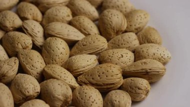 Tüm çiğ badem fıstığını beyaz bir tabakta üst üste yığılmış doğal dokularını yavaşça gösteren kabuklar halinde kapat.