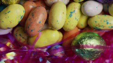 Çeşit çeşit tatlı benekli minik yumurtalar ve folyoya sarılı çikolata yumurtalarının neşeli, parlak, parlak arka plan dokusunda uzanan dönüşümlü manzarası.