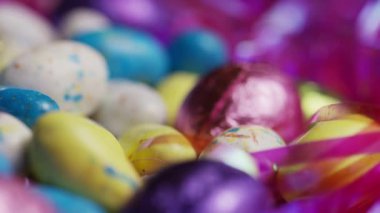 Makro, renkli benekli Paskalya şekerleri yumurtaları ve folyo çikolatalarının yüzeysel alan derinliği ve hafif ışıklandırma detayları ve dokusuyla yakın görüntüsü.