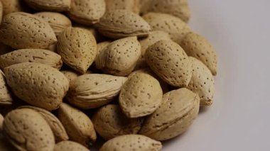 Kabuklu badem yığınları beyaz arka planda dönüyor desenli yüzey ve doğal organik sağlıklı atıştırmalıklar sergiliyor.