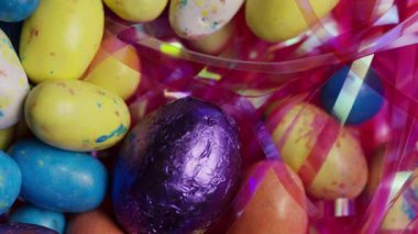 Renkli çikolata kaplı çikolata ve folyoyla kaplanmış yumurta, neşeli bir tatil sahnesi oluşturan parlak festival paketlerinin arasında.