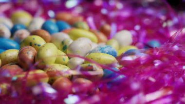 Parlak dekoratif süslemelere saçılmış renkli çikolatalı yumurtalar sığ alan derinliğinde şenlikli bir makro kompozisyon oluşturuyor.