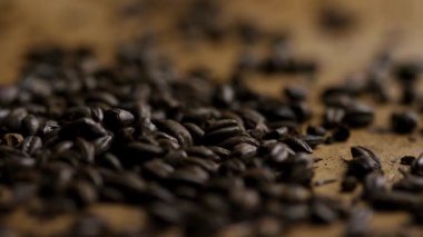Koyu kavrulmuş kahve çekirdekleri sığ derinlik odaklı, kırsal kahverengi yüzeyde üst üste yığılmış.