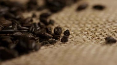Kavrulmuş kahve çekirdekleri kaba çuval bezi yüzeyine saçılmış, kırsal bir doku yaratıyor.