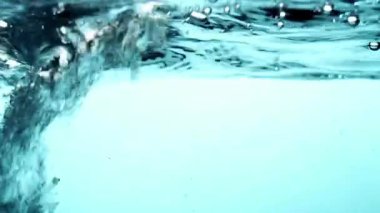 Dalgalanan dalgalar ve kabarcıklar ile turkuaz mavi su yüzeyi hareketli su altı soyut sahnesi oluşturur