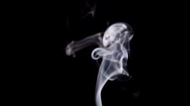 İnce beyaz duman çerçevenin altından dikey olarak yükselir ve siyah bir arkaplan karşısında karmaşık dönen desenlere dönüşür..