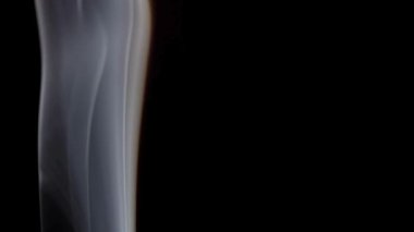 Hassas ve ince bir beyaz duman sütunu, siyah bir arkaplanda yavaşça sallanmadan önce, dikey bir çizgide durmaksızın yükselir..