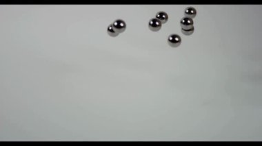 Temiz beyaz bir stüdyo yüzeyinde yuvarlanan ya da zıplayan parlak çelik küreler..