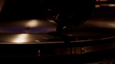 Antika bir gramofon iğnesinin güzel bir yakın çekimi nostaljik ve klasik bir müzik ortamında sıcak alçak ışık altında dönen siyah bir plak çalar.