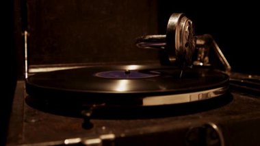 Antik bir gramofonun karanlık bir atmosferik odada plakları çalarken geniş açılı görüntüsü mekanik detayları ve ahşabı aydınlatan bir ışık.