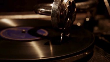 Antika bir gramofon kolu ve iğne kafanın yan görüş açısı karanlık bir odada dönen siyah vinil plağın izlerini takip ediyor.