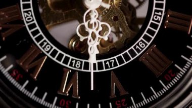 Romen rakamları ve görünür altın iç dişlilerin yer aldığı siyah bir kadranın üzerinde hareket eden beyaz elli mekanik iskelet saat yakın görüntüsü