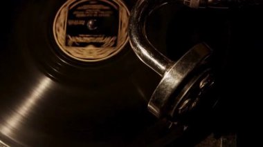 Eski bir gramofoncunun, dönen yivli yüzey üzerinde duran metal iğne koluyla siyah bir plağı döndürürken yukarıdan aşağı bakışı.