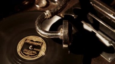 Antika bir gramofon makinesinin, klasik ses ekipmanlarında sıcak spot ışıkları olan karanlık bir odada siyah bir plak çalarken orta ölçekli atmosfer görüntüsü.