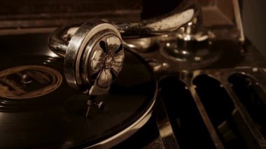 Eskimiş bir gramofon iğnesinin yakın plan görüntüleri karanlık bir odada dönen siyah bir plağın üzerinde sanatsal açıdan sıcak bir yan ışıklandırmayla dinleniyor.