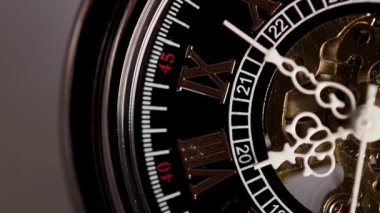 Siyah bir cep saati kadranının kenarına odaklanan aşırı makro. Dakika göstergesi ve elleri dişlilerin üzerinden geçen Roma rakamları.