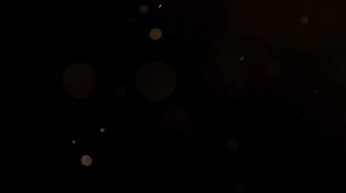 yüzen altın toz parçacıkları ve parıldayan ışık lekeleri karanlık bir arkaplanda yavaşça dans ediyor. Sinema atmosferinde.