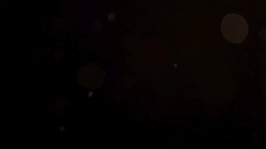 Sinematik yumuşak bokeh ışık daireleri ve küçük titreşimli parçacıklar sihirli ve rüya gibi bir görsel efekt yaratmak için havada siyah bir zemine doğru rastgele sürükleniyorlar.