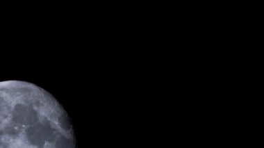 Ayın karanlık gece gökyüzünde yavaşça ilerlerken detaylı görüntüsü çeşitli kraterleri ve ay sıradağlarını gösteriyor.