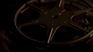 Film projeksiyonu için eski sinematik ekipmanları gösteren koyu renkli arka planda sıcak dramatik ışıklandırmada üst üste dizilmiş klasik film makaralarını kapat