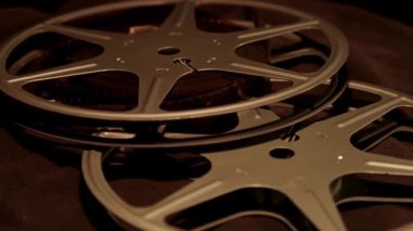 İki klasik gümüş film, sıcak atmosferik stüdyo aydınlatmasında karanlık bir yüzeyde üst üste yatar.