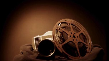 Eski film makaralarının olduğu antika film kamerası karanlık, kapkara bir arka plan stüdyosunun ışıklandırmasına karşı yavaşça dönüyor.